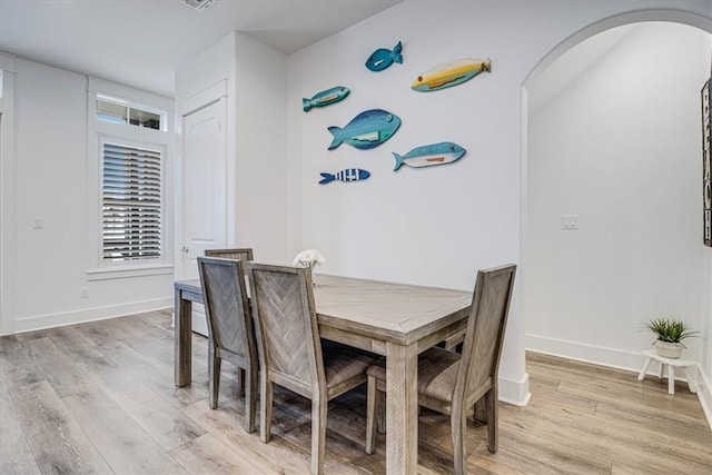 dining area with arched walkways, light wood finished floors, and baseboards