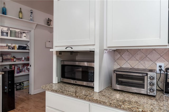 details with a toaster, white cabinets, stainless steel microwave, light stone countertops, and open shelves