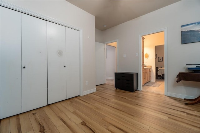 unfurnished bedroom featuring a closet, light wood-type flooring, connected bathroom, and baseboards