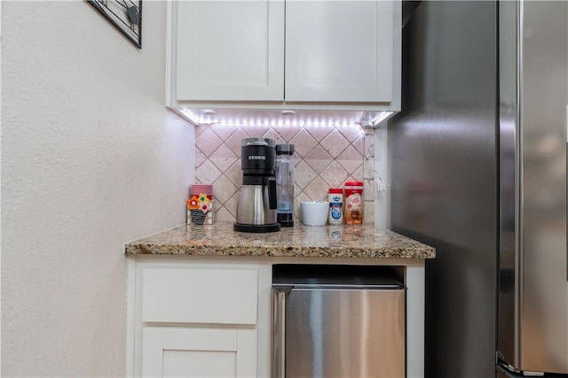 kitchen featuring freestanding refrigerator, light stone countertops, fridge, white cabinetry, and backsplash