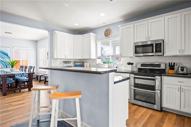678 Anchor Dr, Port Aransas, TX 78373 - kitchen featuring stainless steel appliances, a breakfast bar area, decorative backsplash, light wood finished floors, and dark stone countertops