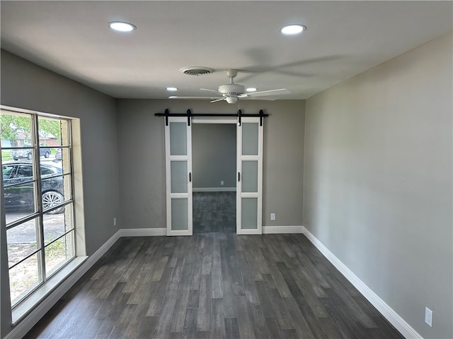 spare room with dark hardwood / wood-style flooring, a barn door, and ceiling fan