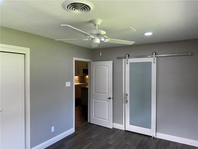 unfurnished bedroom with dark hardwood / wood-style flooring, a barn door, and ceiling fan