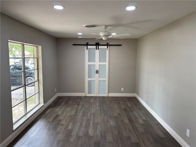 spare room featuring a barn door, dark hardwood / wood-style floors, and ceiling fan