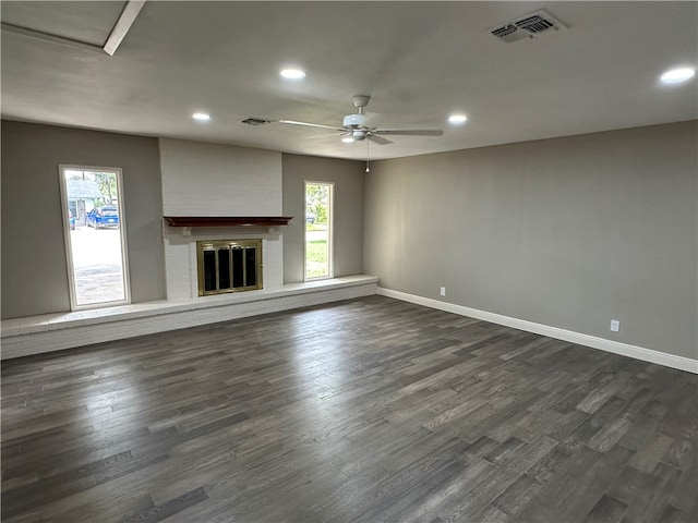 unfurnished living room featuring dark hardwood / wood-style flooring, ceiling fan, and a brick fireplace