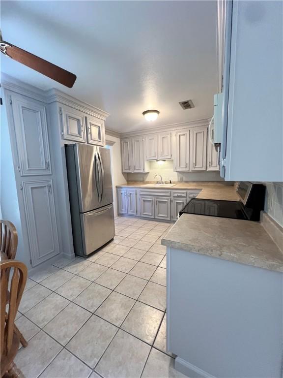 kitchen with light tile patterned floors, freestanding refrigerator, a sink, light countertops, and crown molding