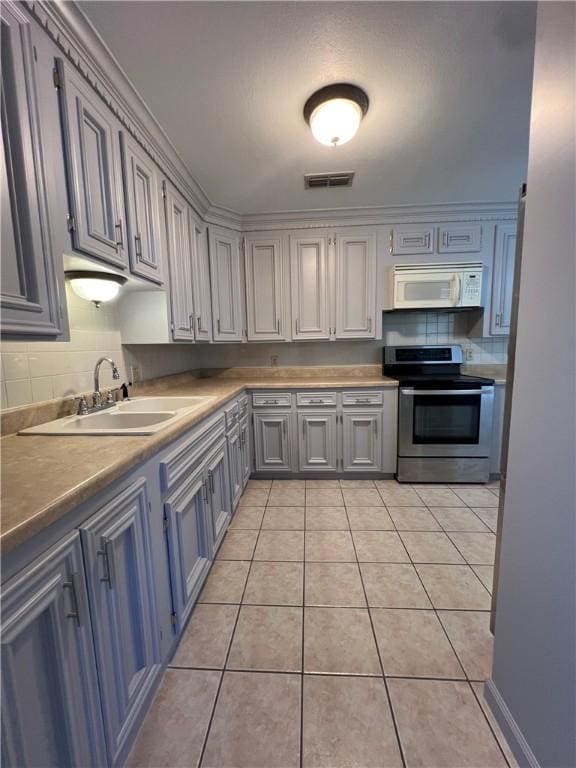 kitchen featuring light tile patterned floors, white microwave, visible vents, a sink, and stainless steel range with electric cooktop