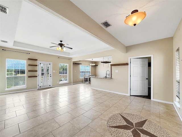 unfurnished living room featuring sink, ceiling fan with notable chandelier, a tray ceiling, and light tile patterned flooring