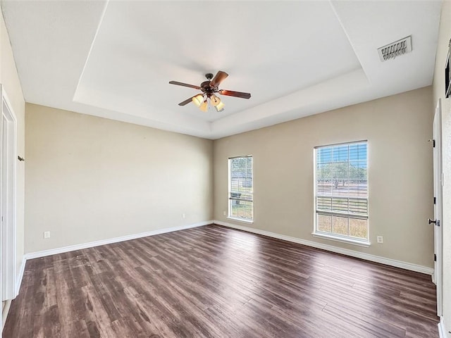 spare room with a raised ceiling, ceiling fan, and dark wood-type flooring