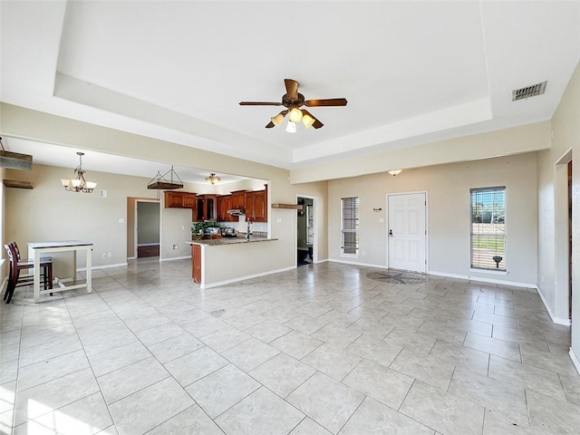 unfurnished living room featuring a tray ceiling and ceiling fan with notable chandelier