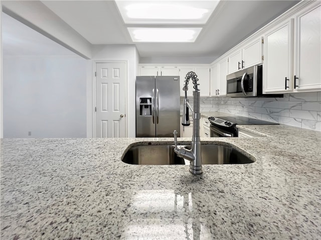 kitchen featuring sink, tasteful backsplash, light stone countertops, white cabinetry, and appliances with stainless steel finishes