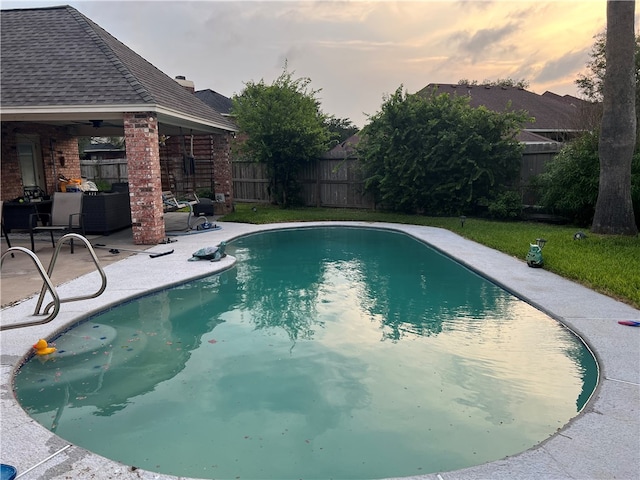 pool at dusk featuring ceiling fan and a patio area