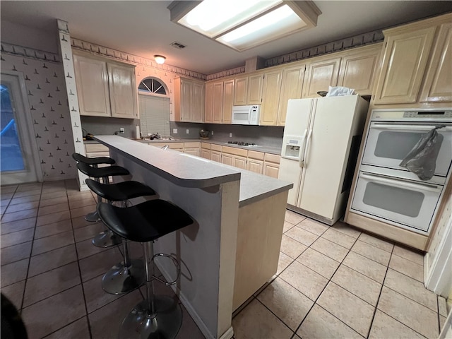 kitchen with light tile patterned flooring, sink, a breakfast bar, white appliances, and a kitchen island