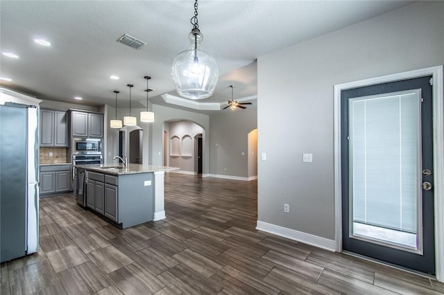 8022 Calgary Dr, Corpus Christi, TX 78414 - kitchen with stainless steel appliances, arched walkways, gray cabinetry, ceiling fan, and decorative backsplash