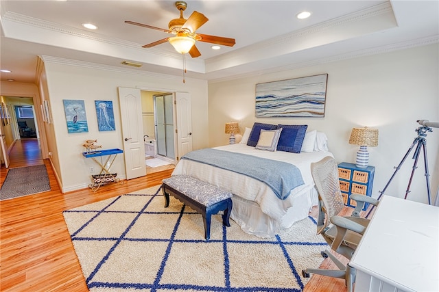 bedroom with wood-type flooring, ensuite bath, crown molding, a tray ceiling, and ceiling fan