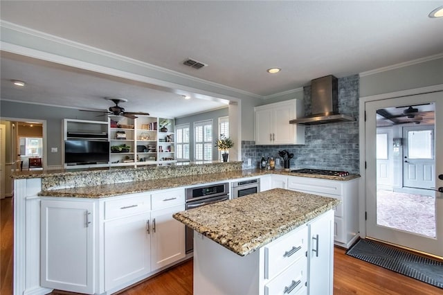 261 Louisiana Ave, Corpus Christi, TX 78404 - kitchen with wall chimney range hood, a ceiling fan, wood finished floors, a peninsula, and a center island