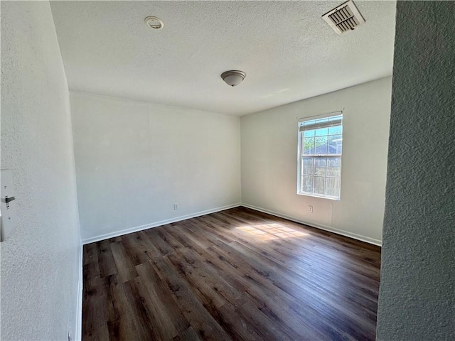 spare room with a textured ceiling, visible vents, wood finished floors, a textured wall, and baseboards