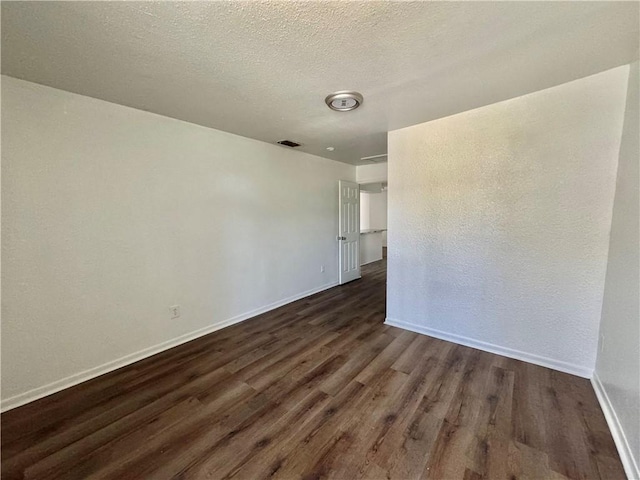 empty room featuring dark wood-style floors, baseboards, visible vents, and a textured ceiling