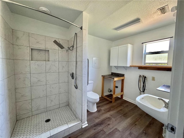 bathroom featuring a textured ceiling, visible vents, toilet, wood finished floors, and a stall shower