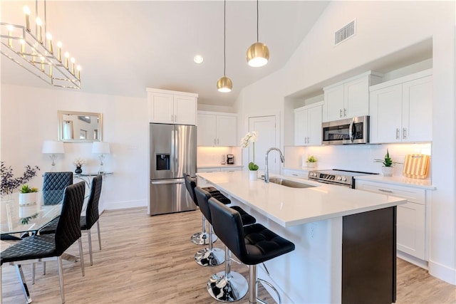 kitchen with appliances with stainless steel finishes, a sink, light wood-style floors, backsplash, and high vaulted ceiling