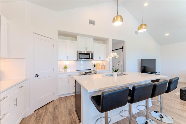 kitchen featuring stainless steel appliances, a sink, a kitchen bar, light wood-style flooring, and white cabinetry