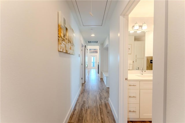 corridor featuring attic access, a sink, wood finished floors, and baseboards