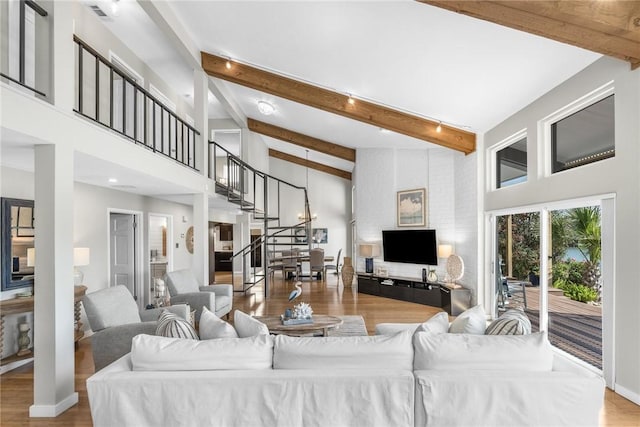 living room with beam ceiling, stairway, wood finished floors, and a high ceiling