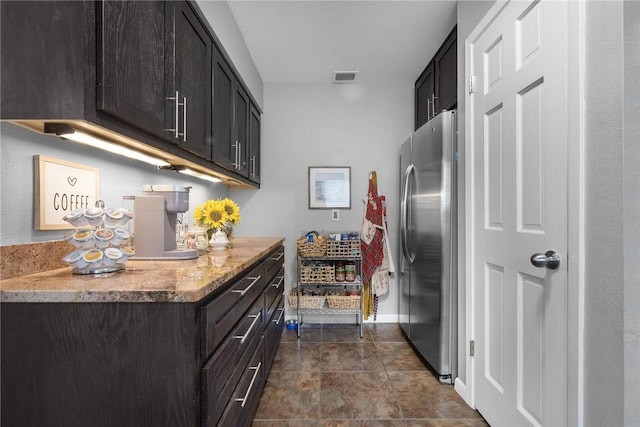 kitchen with visible vents, baseboards, dark tile patterned floors, and freestanding refrigerator