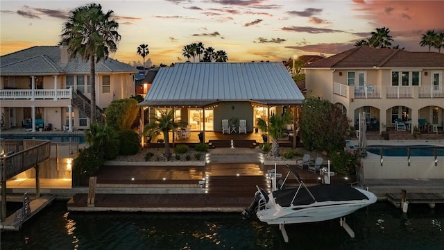 back of house at dusk featuring stucco siding, a water view, a standing seam roof, an outdoor pool, and metal roof