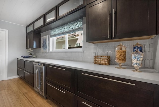 kitchen with beverage cooler, light countertops, dark brown cabinetry, glass insert cabinets, and light wood-style floors