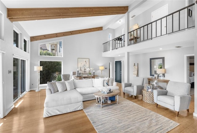 living room featuring beamed ceiling, a high ceiling, visible vents, and wood finished floors