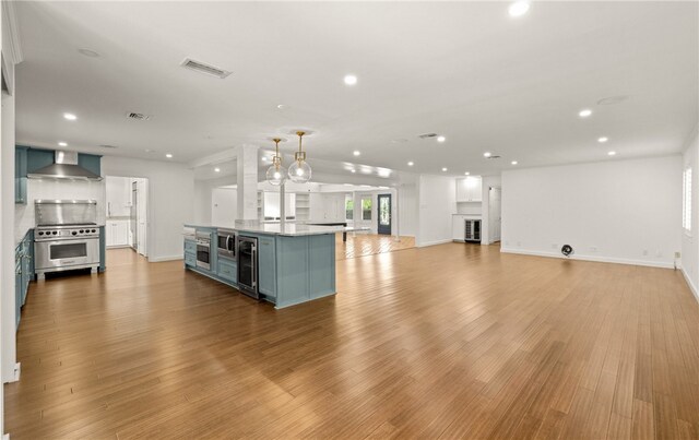 kitchen with light hardwood / wood-style floors, wall chimney exhaust hood, a kitchen island, high end stainless steel range, and decorative light fixtures