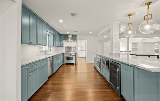 kitchen with stainless steel appliances, wine cooler, wall chimney range hood, decorative light fixtures, and dark hardwood / wood-style floors