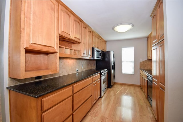 kitchen featuring dark stone countertops, baseboards, stainless steel appliances, light wood-style floors, and backsplash