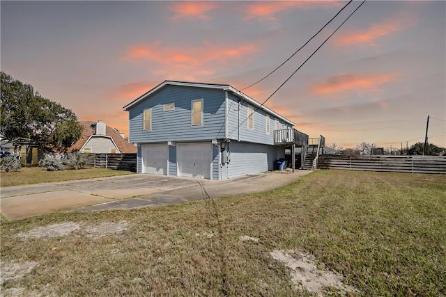 property exterior at dusk with a lawn, fence, concrete driveway, a garage, and stairs