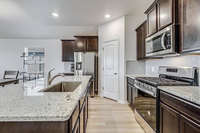 kitchen with a kitchen island with sink, sink, light stone countertops, appliances with stainless steel finishes, and light hardwood / wood-style floors