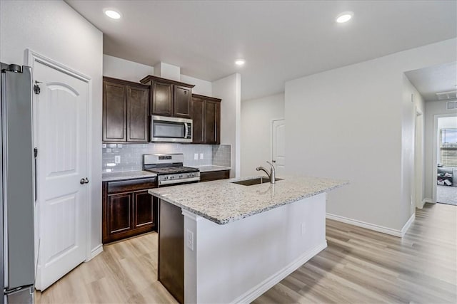 kitchen with light stone countertops, a center island with sink, stainless steel appliances, and a sink