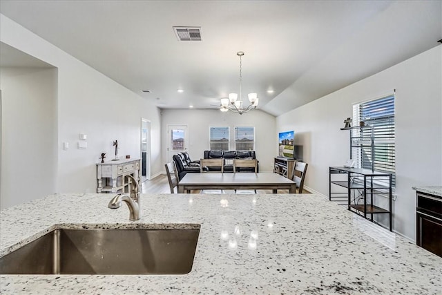 kitchen featuring light stone counters, visible vents, hanging light fixtures, a sink, and a chandelier