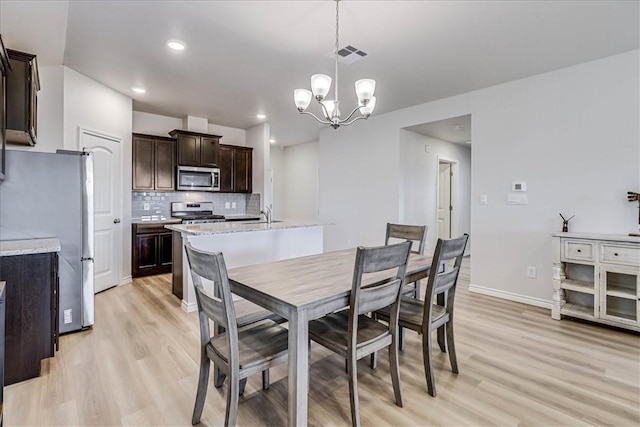 dining space with baseboards, visible vents, a notable chandelier, and light wood finished floors