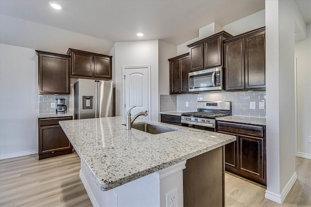 kitchen with stainless steel appliances, light stone counters, a sink, and a kitchen island with sink