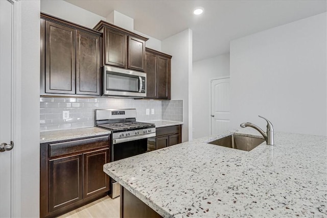 kitchen with light stone counters, sink, light wood-type flooring, and appliances with stainless steel finishes