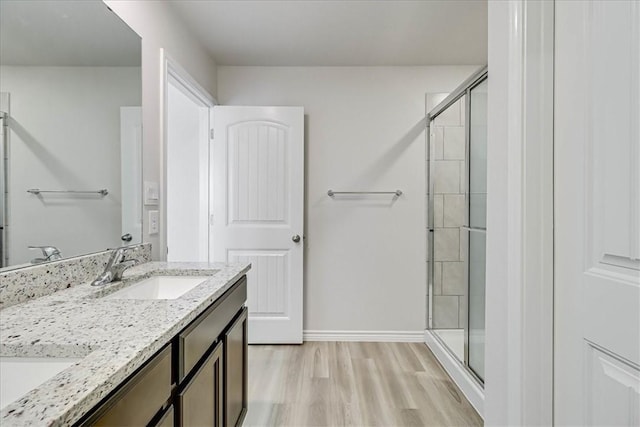 bathroom featuring wood finished floors, a sink, baseboards, double vanity, and a stall shower