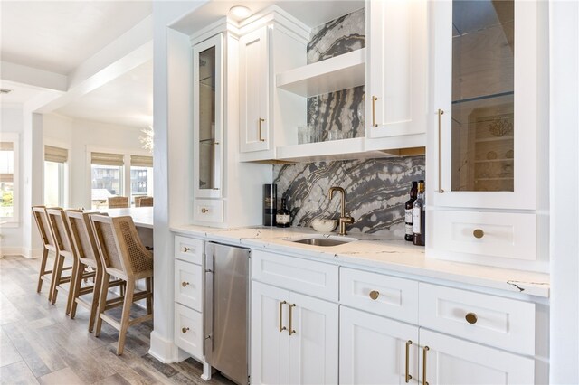 bar featuring light stone counters, white cabinets, decorative backsplash, sink, and light hardwood / wood-style flooring