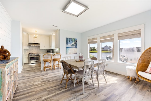 dining area featuring light hardwood / wood-style flooring, a water view, and an inviting chandelier