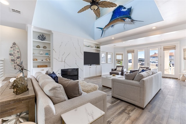 living room featuring french doors, a towering ceiling, hardwood / wood-style flooring, a premium fireplace, and ceiling fan