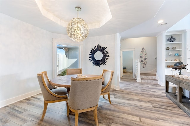 dining area featuring an inviting chandelier, built in features, light hardwood / wood-style flooring, and a tray ceiling