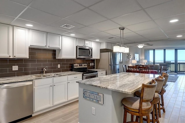 kitchen with stainless steel appliances, sink, light stone countertops, a drop ceiling, and a center island