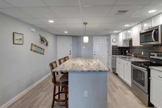 kitchen featuring stainless steel appliances, pendant lighting, white cabinets, a breakfast bar, and a center island