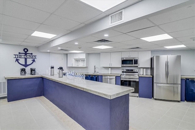 kitchen featuring white cabinets, kitchen peninsula, a drop ceiling, and stainless steel appliances