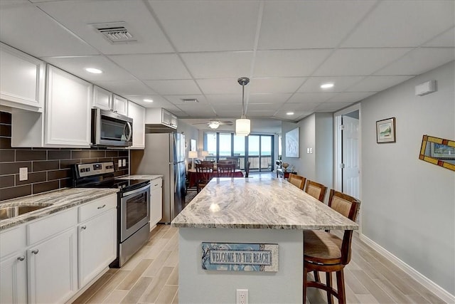 kitchen featuring pendant lighting, appliances with stainless steel finishes, white cabinetry, tasteful backsplash, and a kitchen breakfast bar